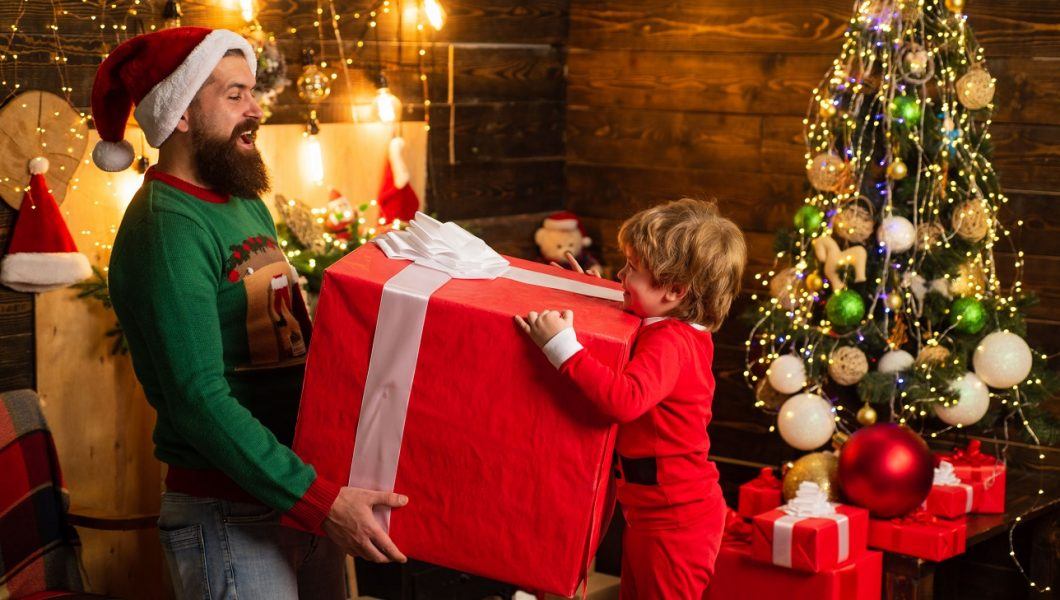 Cute little child with parent is decorating the Christmas tree indoors. Home Christmas atmosphere. Christmas kids with gift emotion - happiness concept.