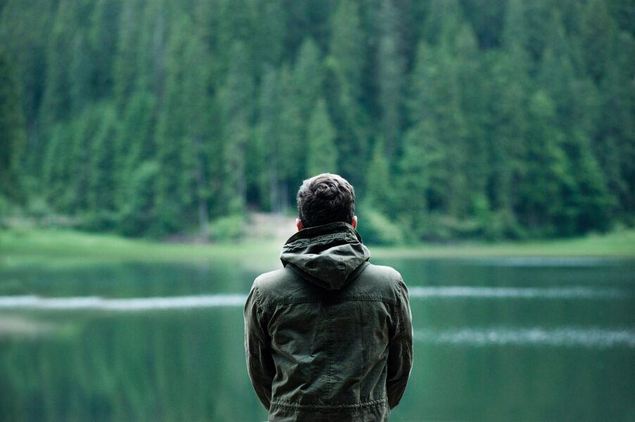 man in green hoddie overlooking lake with trees in background