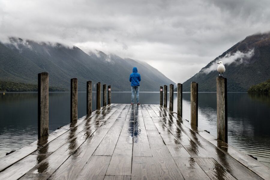 person standing at the end of a wet dock overlooking lake and mountains