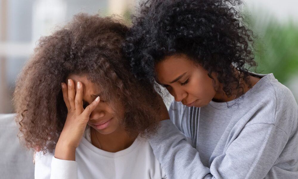 two young black women grieving comforting each other