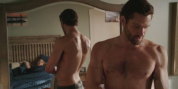 Jared Padalecki looking down with shirt off at Geri in bed on Walker set.